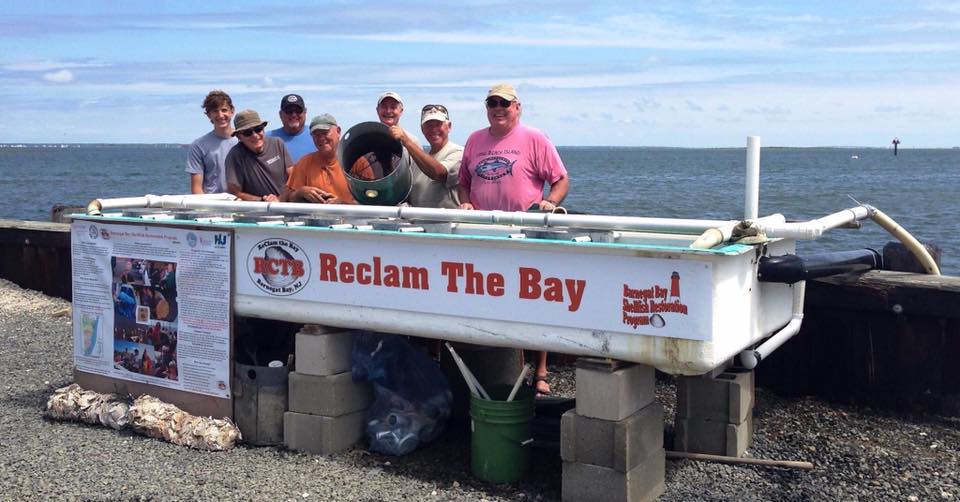 A group of volunteers with 'ReClam the Bay' pose next to an upweller. (Photo: RCTB)